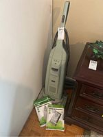 Full view of light gray upright Kenmore Elegance vacuum and three unopened vacuum bags on floor next to it.