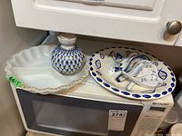 Widely shows all items including vase, divided serving dish, plate, and soup spoons on a microwave oven.