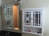 View of white wall cabinet with glass paneled double doors, and lower open shelf with decorative items.