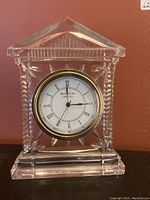 Front view showing clear crystal mantel clock with triangular pediment and round clock face with Roman numerals and Waterford Crystal branding