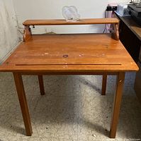 Front view of a wooden children's art desk showing the tabletop with signs of wear and the raised shelf on the rear edge. The wood has visible scratches and discoloration from use.