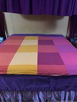 King size bed with colorful patchwork-style bedding in purple, orange, yellow, red, and pink tones.