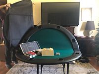 Poker table topper half-folded, showcasing green felt playing surface, black padded rim with six cup holders, and carrying case held open by a person