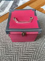Photo of closed pink and black box with handle and latch containing 45 RPM vinyl records.