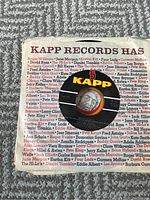 Photo showing a 45 RPM record in a Kapp Records branded sleeve listing multiple 1960s artists on the back cover.