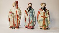 Front view of three Chinese wise men porcelain figurines showing detailed hand-painted robes and facial expressions.