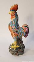 Full side view of the colorful hand painted porcelain rooster figurine on stand.