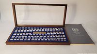 Open wooden display case with blue interior showing 142 silver ingots and booklet placed beside case