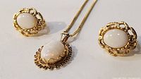 Close-up of pendant and earrings on white surface showing opal centers and decorative gold surrounds