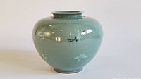 Front view of the pale green Korean celadon moon jar with crackle glaze and decorative black and white marks.