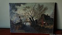 Full view of the oil painting on canvas depicting a dark landscape with a bridge and cottage, showing surface crackling and wear.
