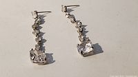 Pair of sterling silver drop earrings laid flat showing the full length and multiple clear stones including one large square stone on each earring.