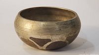 Side angle of the brass singing bowl showing etched designs on lower half and patina on the surface.