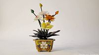 Front view of decorative jade flower arrangement in cloisonné planter on white background