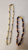Both necklaces laid out showing the mother-of-pearl and lapis beads necklace and the amber necklace side by side.