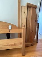 Disassembled pieces of solid pine wood double bed frame showing headboard, footboard, and side rails stacked and leaning against a wall.