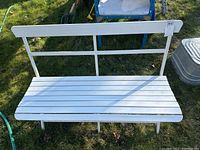 Front view of white outdoor folding bench with metal frame and wood slats, placed on grass.