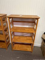 Front view of wooden bookcase with four shelves, natural light brown finish and vertical supports on the sides