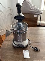 Electric Breville citrus juicer with lever arm pressed down partially on wood table, showing stainless steel reamer and power cord extending out.