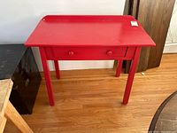 Red wooden desk with one drawer closed, showing the top and front view with a tag on the top right corner.