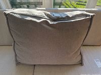 Grey dog bed placed on light grey couch with visible zipper and fabric texture under natural light.