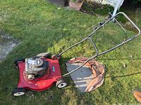 Full side view of red Briggs & Stratton gas lawn mower with metal handlebar and attached beige grass catcher bag, showing overall condition.