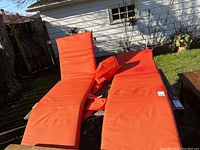 Two red-orange adjustable lounge chairs positioned outdoors on a table in backyard, showing full length and adjustable backs.