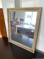 Full view of the rectangular cream and gold framed mirror placed on a dark surface showing reflective glass and frame details.