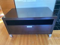 Front view of the wooden TV stand showing open shelf and storage drawer with metal handle, placed on wood flooring.