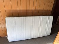 Front view of white twin mattress leaning against wood-paneled wall in basement.