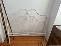 White metal headboard leaning against wall showing curved and circular decorative metalwork with paint chipping.