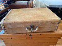 Full view of the top and one side of the vintage suitcase showing worn leather surface and metal edge reinforcement.