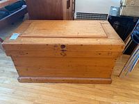 Full view of wooden chest showing front and side with natural light wood finish and signs of wear.
