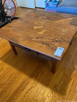 Front view of square wooden coffee table showing geometric patterned top with inlaid fish designs and surface wear.