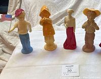 Four Avon figurine perfume bottles standing side by side on a white cloth background. Each about 9 inches tall, untested, some may contain perfume.