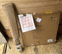 Photo showing two boxed items side by side on wood floor against wall. One box labeled Stonebriar mirror, the other package is rolled drying rack.