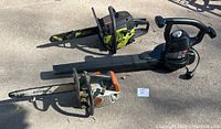 Three power tools arranged on concrete: orange and white Stihl gas chainsaw with 15-inch bar, green and black Poulan gas chainsaw with 14-inch bar, and black Toro electric leaf blower, showing general condition and appearance.