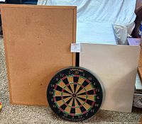Photo showing all three items: dart board, cork board, dry erase board placed on carpet in front of a white backdrop and sofa.