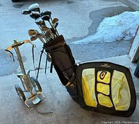 Older metal golf cart, black golf bag with miscellaneous golf clubs, and portable pitching net on the ground.