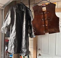 Photo showing both the black leather trench coat and the brown medieval style vest hung side by side, full view.