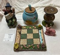 Front view of six ceramic and wooden decorative items including a man figurine, vacation fund jar, wooden candlestick, rabbit figurine, and square tile with animal figures.
