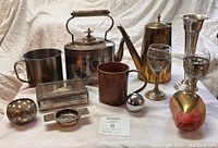 Front view of the lot showing all items including teapot, mugs, coffee pot, goblets, jewelry box, decorative apple, and small accessories.