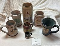 Front and angle view of seven beer steins arranged in two rows, showing details of Oktoberfest and Renaissance designs