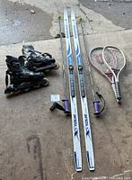 Photo showing rollerblades, cross-country skis with poles, and two tennis rackets laid out on ground.