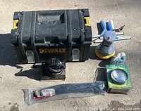 Photo showing Dewalt toolbox, orbital sander, buffer, utility light in packaging, large zip ties, and squeegees arranged on concrete floor