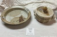 View of two vintage handmade ceramic stoneware pieces: a decorative plate bowl on the left and a covered casserole dish on the right on cloth background.