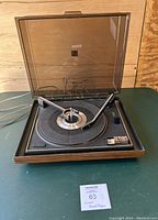 Vintage Magnavox record player open with tonearm and visible controls on green surface.