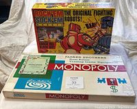 Showcases boxed Mattel Rock'em Sock'em Robots game and the 1961 Parker Brothers Monopoly boxed game together on a plain background.