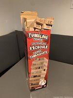 Image of the unopened branded box showing the Tumbling Tower game with numbered wooden blocks visible inside.