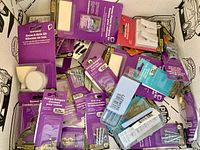 Photo shows various new hanging materials including screw-in hooks, adhesive hooks, picture hangers, nails, felt pads for wall protection, all in their original packaging mostly purple and blue retail packs.